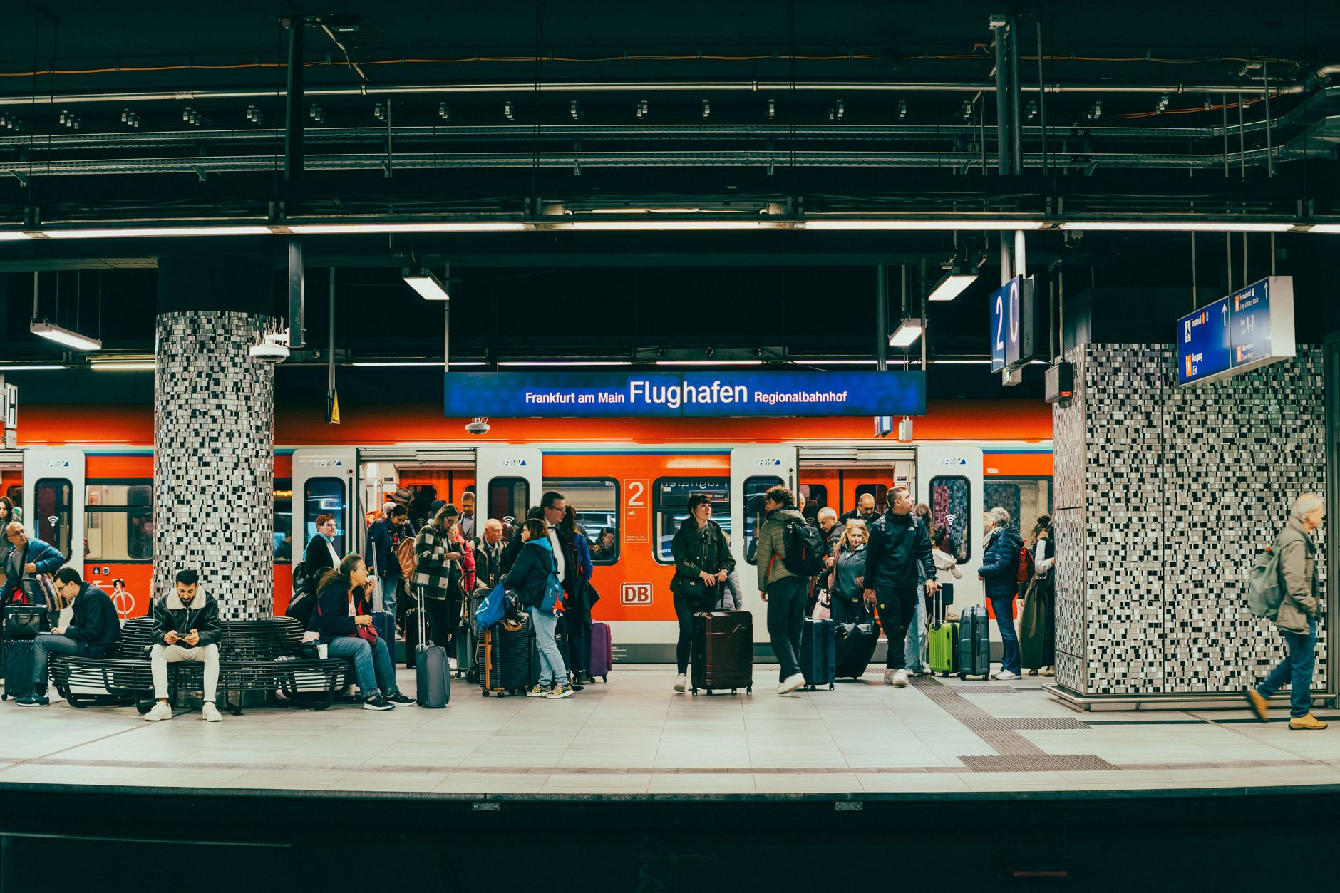 Passengers wait on the platform at Frankfurt am Main Flughafen train station with a regional train in the background.