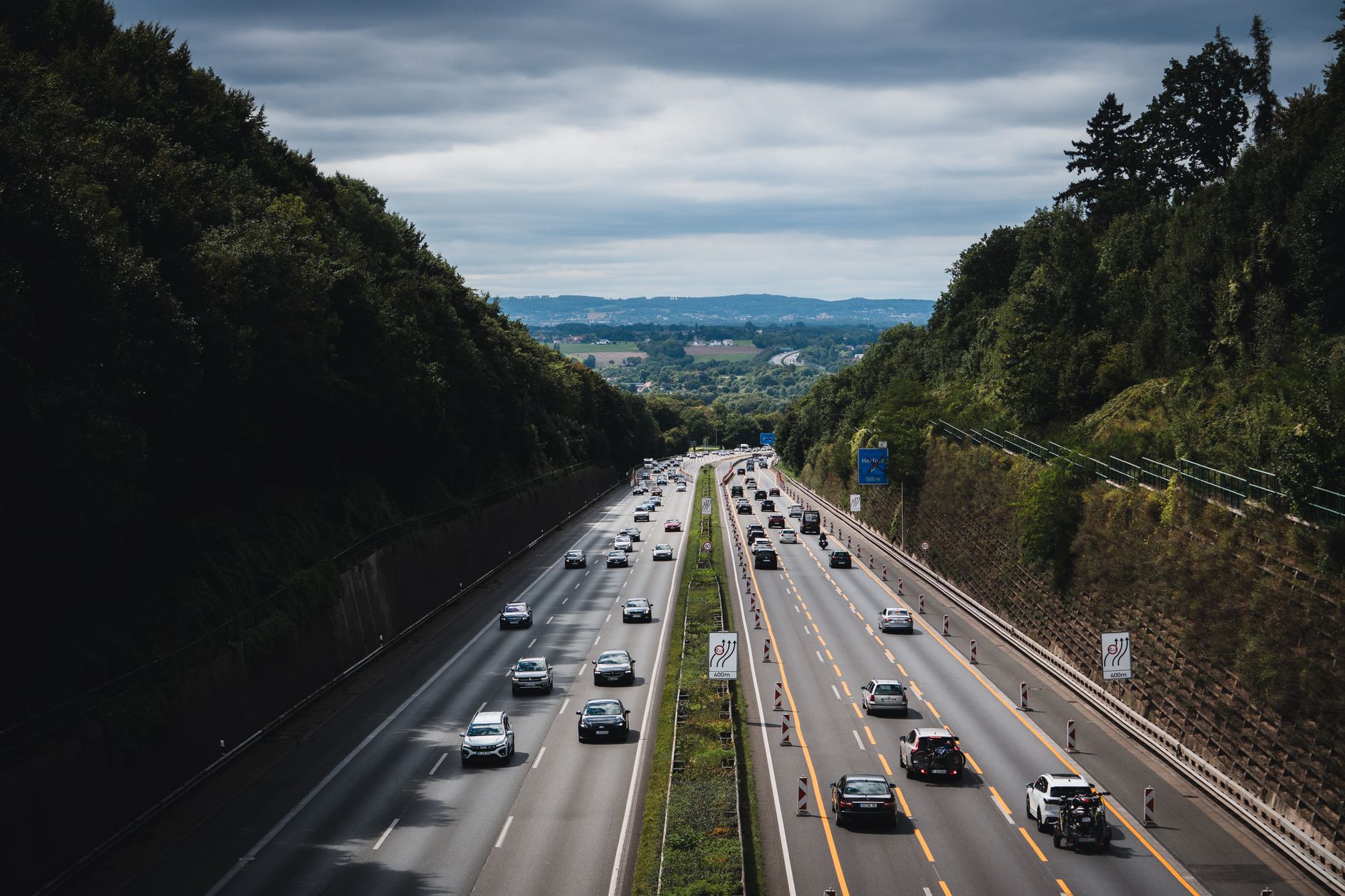 A bustling highway cuts through lush forests under a cloudy sky in Herford, Germany.
